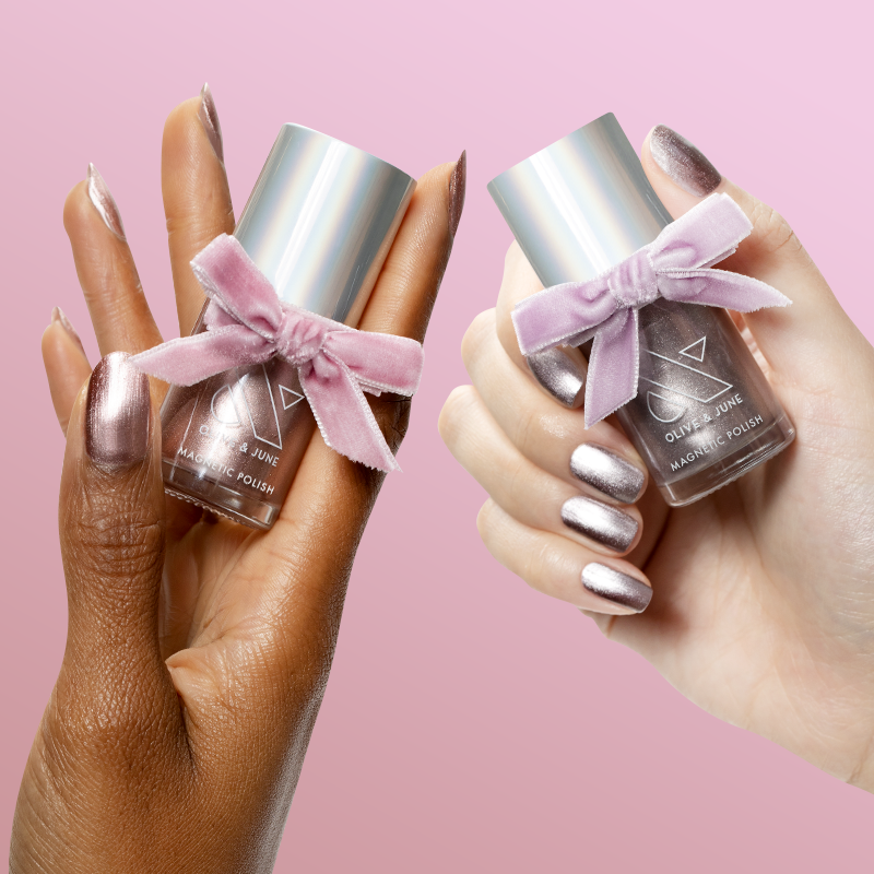 Two hands holding Pretty Neutral Velvet Duo bottles with velvet bows and matching manicured nails against pink background