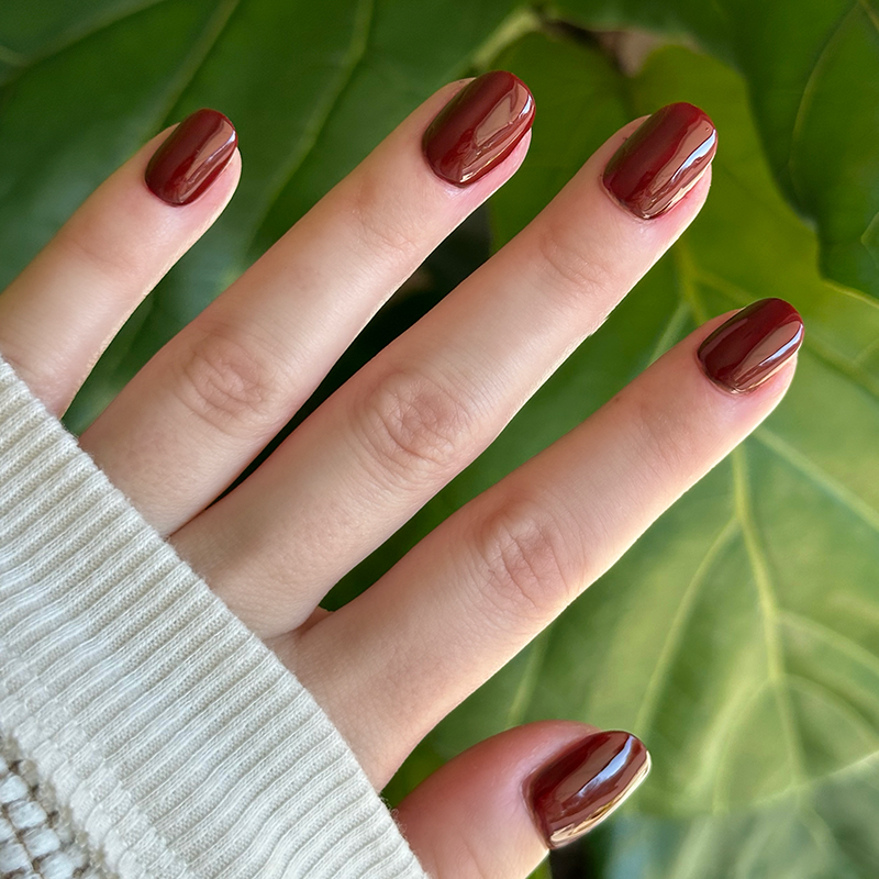 Hand with short rounded nails painted in deep cherry red from Chocolate Cherry manicure by Olive and June outdoors
