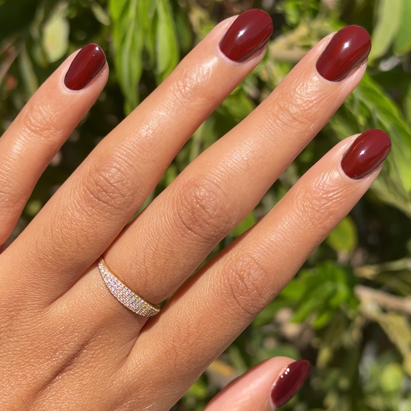 Hand with medium-length nails painted in deep cherry red shade from Chocolate Cherry manicure set outdoors