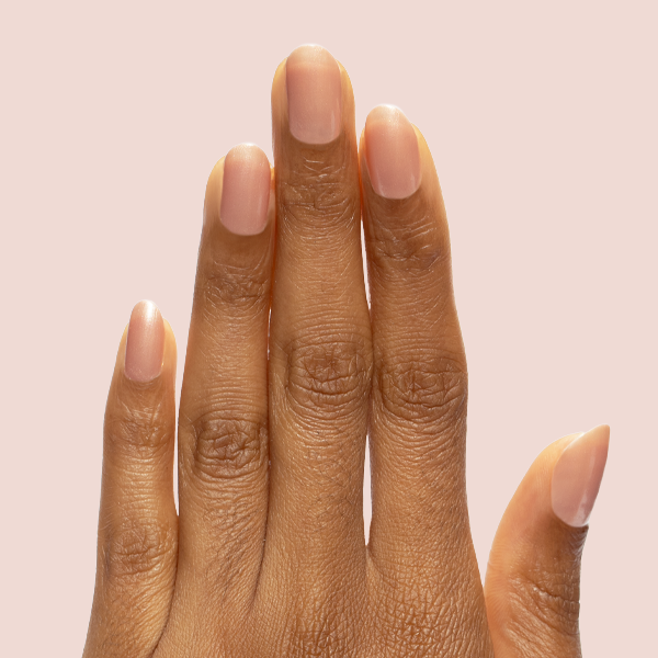 Hand with short natural nails polished in Cookie Swap shimmery beige champagne shade against light pink background