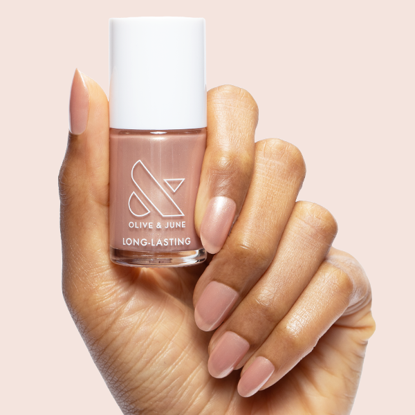 Hand with natural medium-length nails painted in Cookie Swap polish holding Olive and June long-lasting nail polish bottle