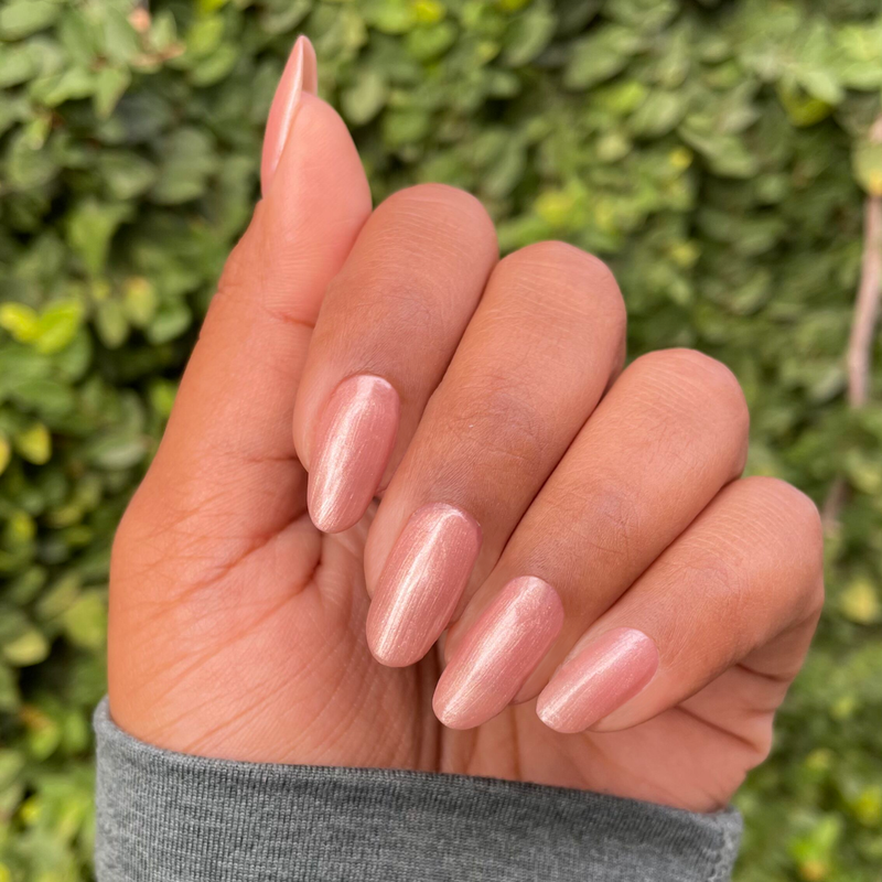 Fingers with almond-shaped nails painted in shimmery Cookie Swap gel polish against a leafy background