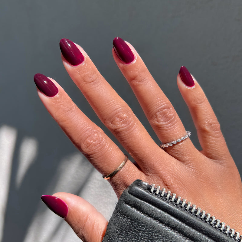 Hand with warm medium skin tone wearing Luxe Loafer gel polish in deep crimson jelly for a shiny, long-lasting manicure outdoors