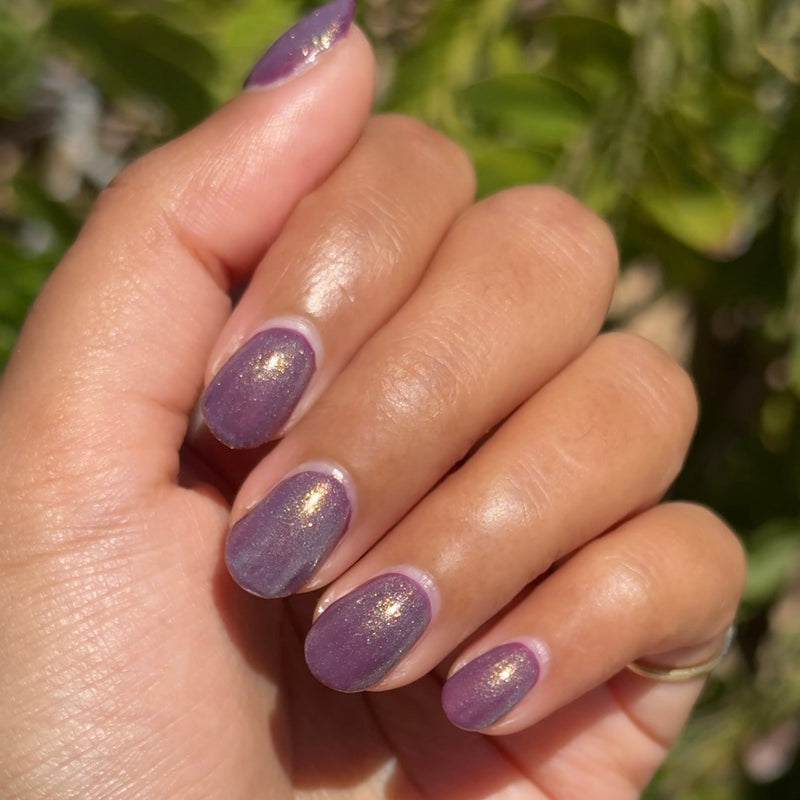 Hand with medium oval nails painted in shimmering purple with gold flecks from Sugar Plum Fairy manicure set outdoors
