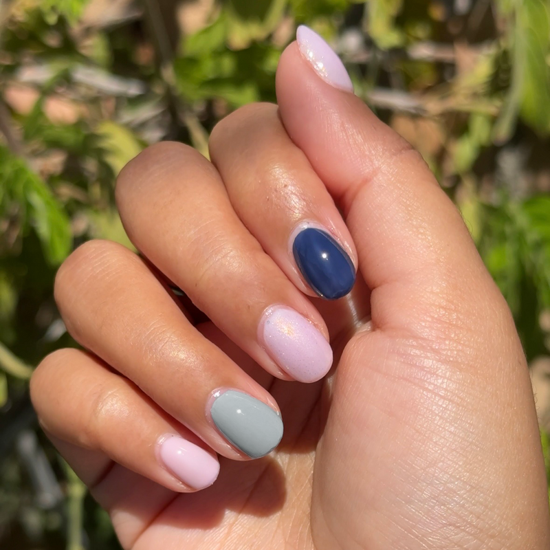 Hand with short oval nails painted in blue, gray, and sheer pink shades from Sweet Dreams mani set outdoors