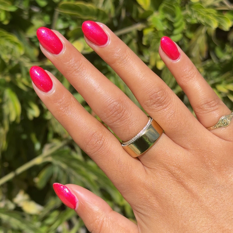 Hand with shimmering bright ruby red mani using Rodeo Ruby polish shown against green foliage background