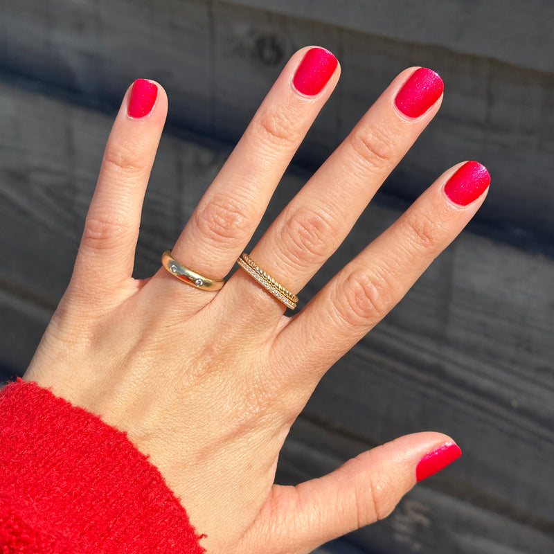 Hand with glossy shimmery bright red manicure in Rodeo Ruby polish shown in natural light against neutral background
