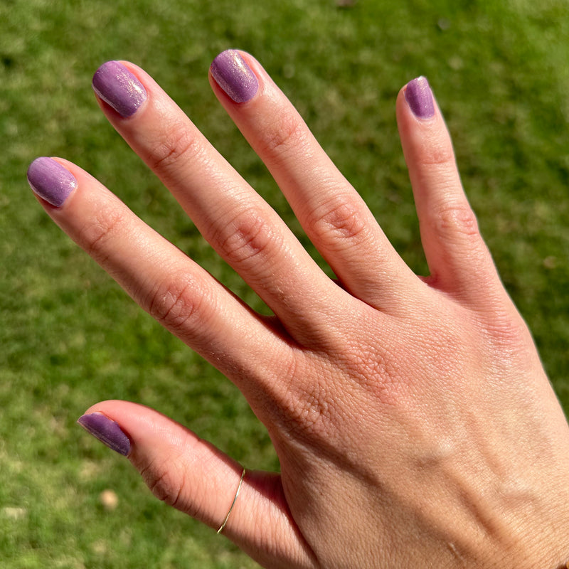 Hand with short natural nails painted in shimmering purple polish from Sugar Plum Fairy for a subtle mani outdoors