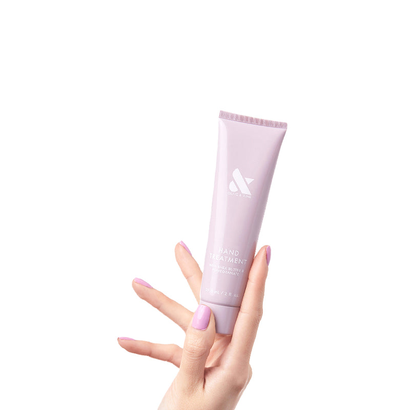 Hand with lilac manicure holding pink tube of HAND TREATMENT cream for hydration and skin renewal on white background