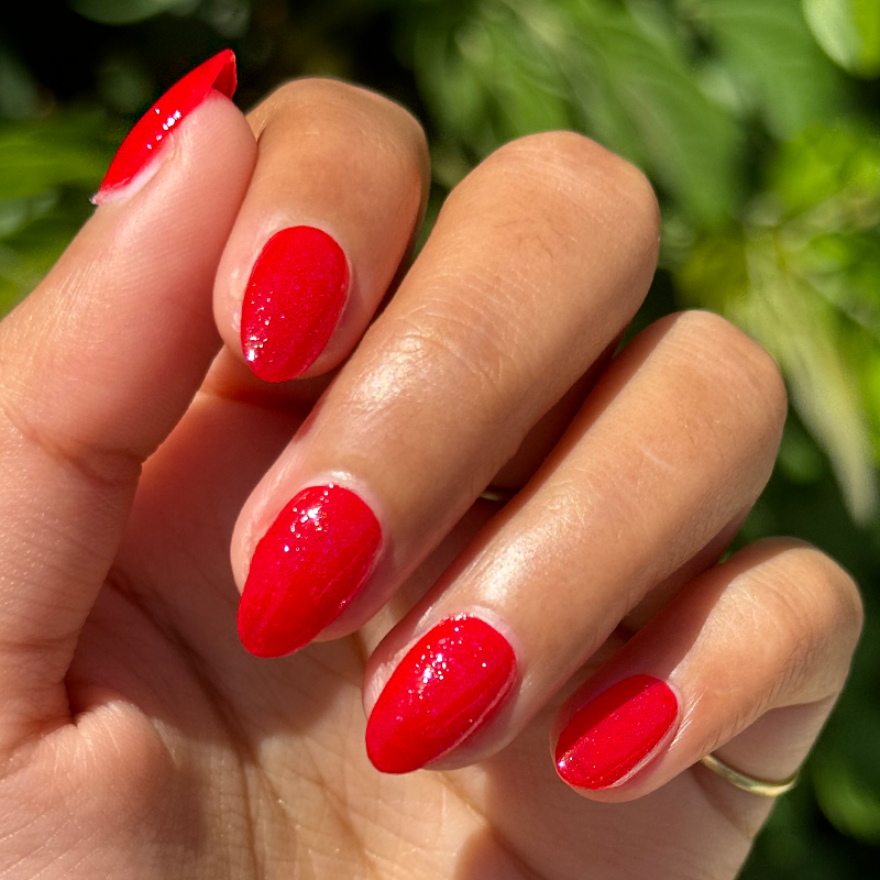 You’re a Firework Set featuring glossy bright red nails with subtle sparkles on natural hand outdoors in sunlight