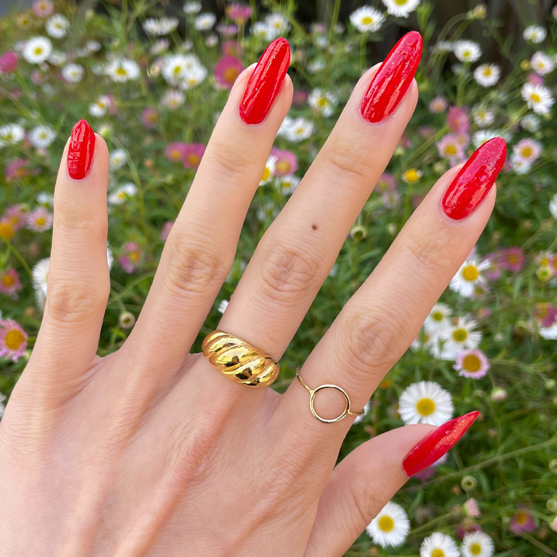 You’re a Firework Set featuring glossy candy red manicure with subtle sparkle accents on natural hand over floral background