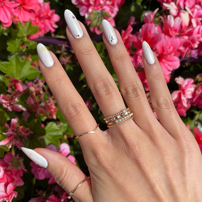Be a Star Set featuring pearl white manicure with metallic star nail art on natural hand outdoors by pink flowers