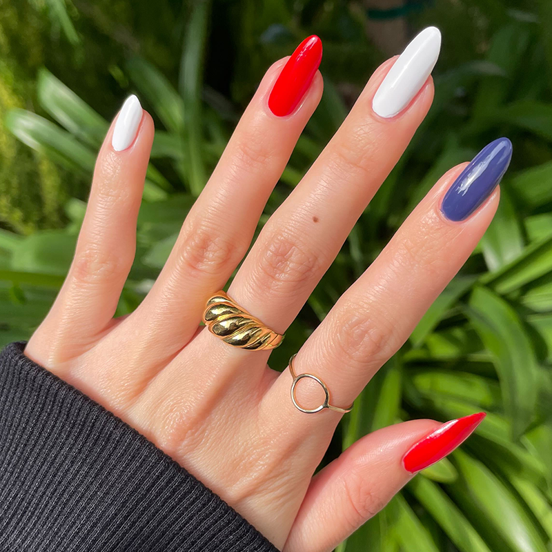 Festive Flag Set showing glossy red, white, and blue manicure on natural hand with gold rings outdoors in sunlight
