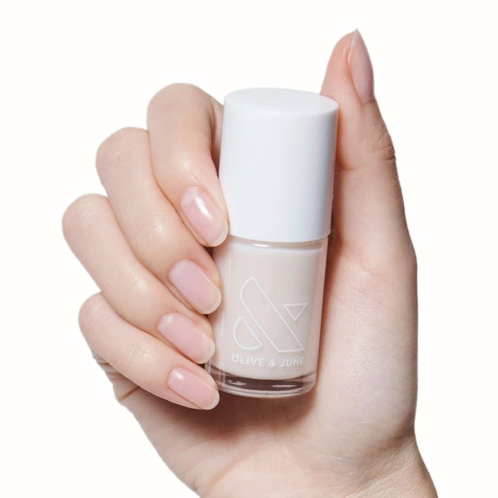 Hand holding a sheer, pale pink nail polish bottle from The Sheer Set for natural-looking at-home manicures