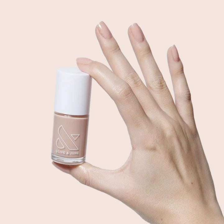 Hand holding a neutral pink polish bottle from The Sheer Set showcasing a glossy natural mani finish