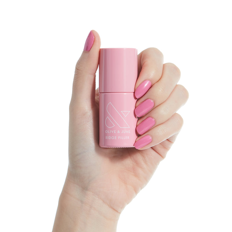 Hand with pink manicured nails holding a pink Olive and June Ridge Filler bottle for smoother nail ridges