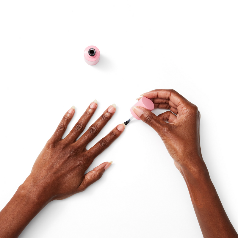 Hand applying Ridge Filler with brush to natural nails on dark skin tone for smooth manicure prep