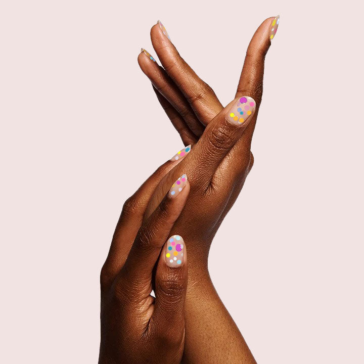 Hands with nails decorated in colorful dots using Sprinkle Cookie polish on neutral light background for mani