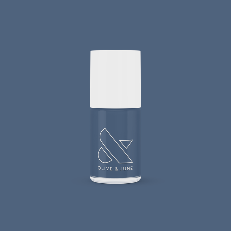 Olive and June nail polish bottle in Social Studies deep navy shade with white cap on matching blue background