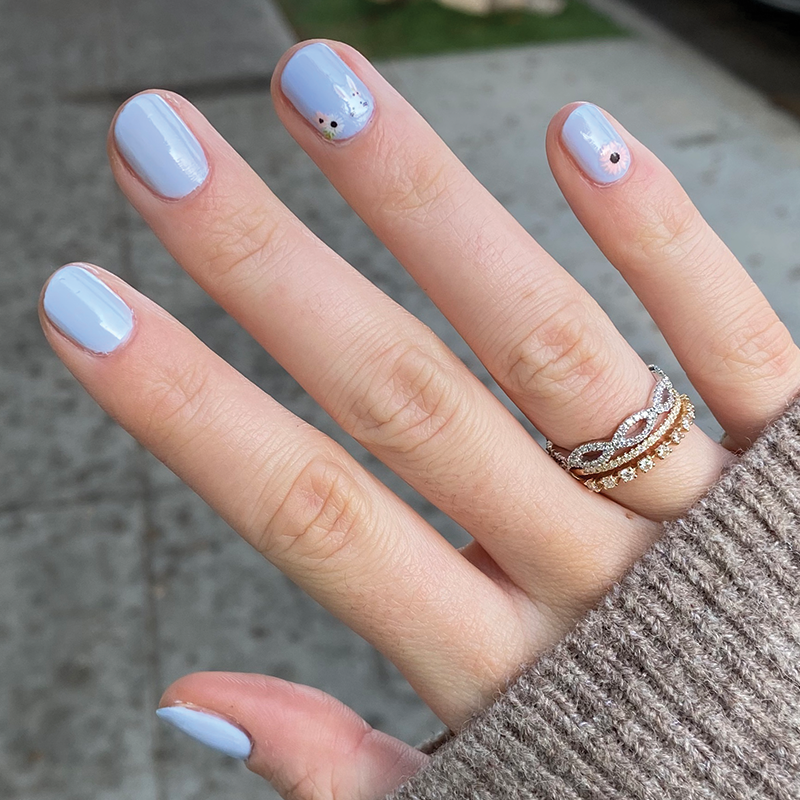 Hand with nails painted in BP, a pastel icy light blue gel polish with delicate floral accents for a fresh manicure