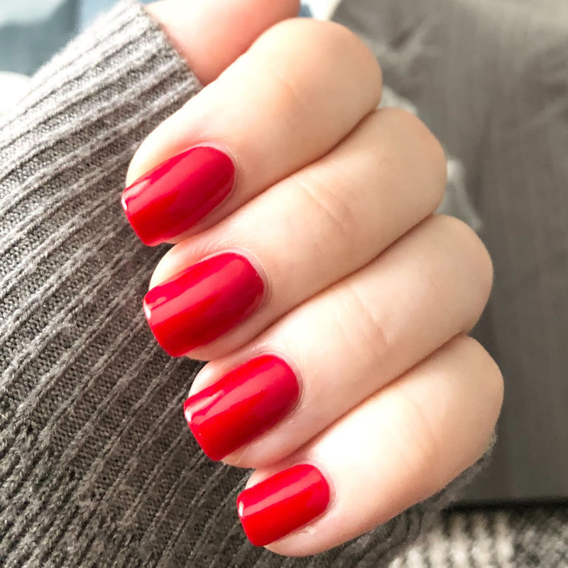 Hand showing glossy nails painted with CV bright cherry red polish from Olive and June for a classic mani look
