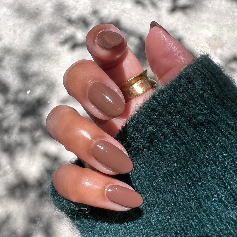 Tip Your Barista almond-shaped nails polished in rich espresso brown shown in natural sunlight with gold ring and green sweater