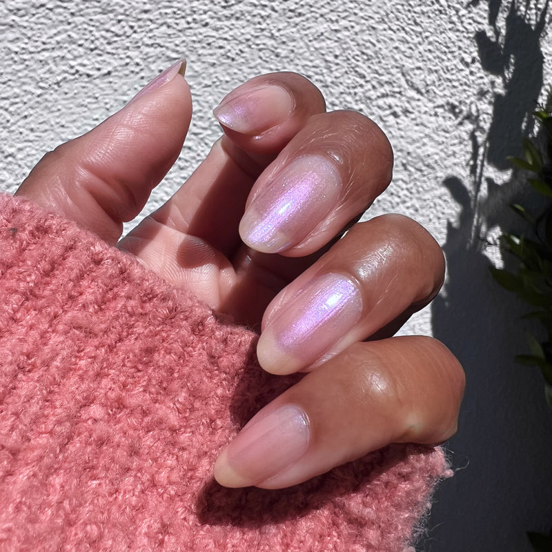 Hand with medium-length natural nails coated in Baroque gel polish showing subtle pearly iridescent shine outdoors