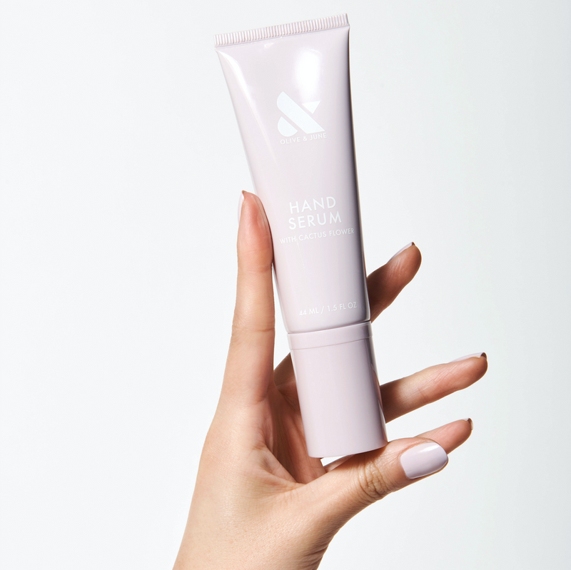 Hand holding a pale pink tube of Hand Serum with manicured nails in a soft neutral polish shade