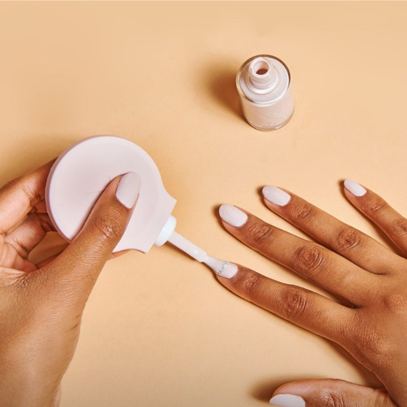 Hand applying light nude polish with The Poppy universal bottle handle for easy at-home mani control