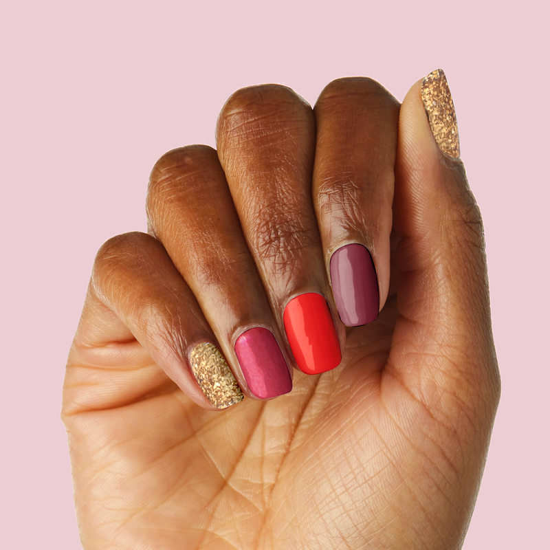 Hand with Cranberry Spritz manicure in shades of ruby, bordeaux, bright red, and sparkling gold polish on natural nails