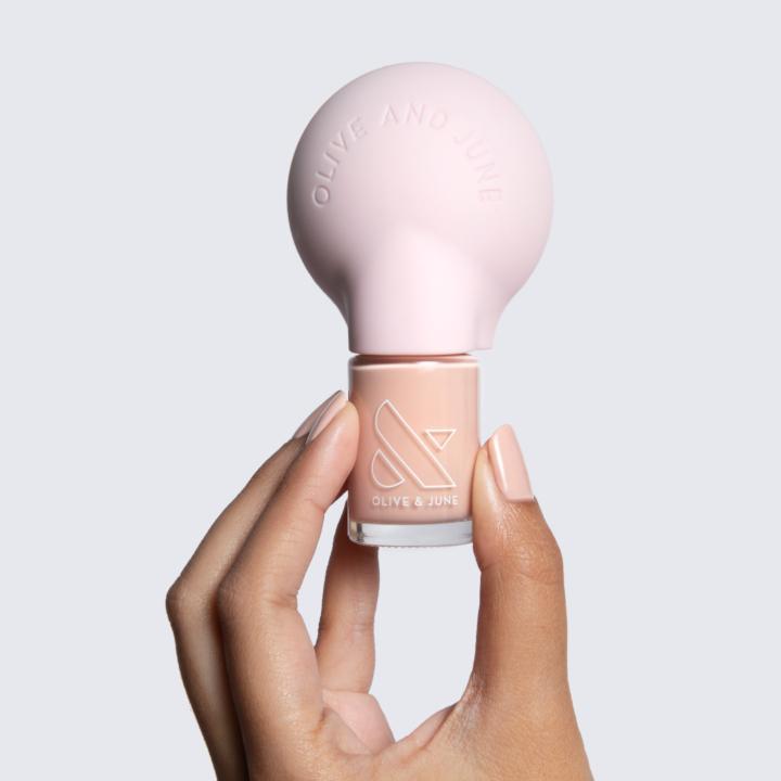 Hand holding The Poppy universal nail polish bottle handle with nude polish for easier at-home manicure control