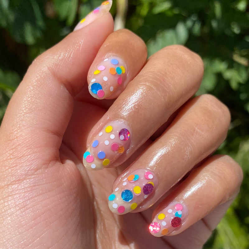 Hand with nails featuring a colorful sprinkle design using Sprinkle Cookie polish in natural light outdoors