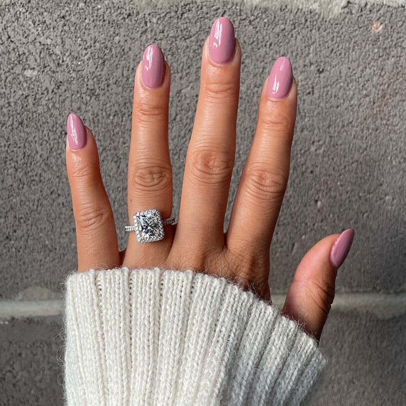 Hand with glossy World Lit nail polish in mauve shade wearing a diamond ring and cozy white sweater cuff