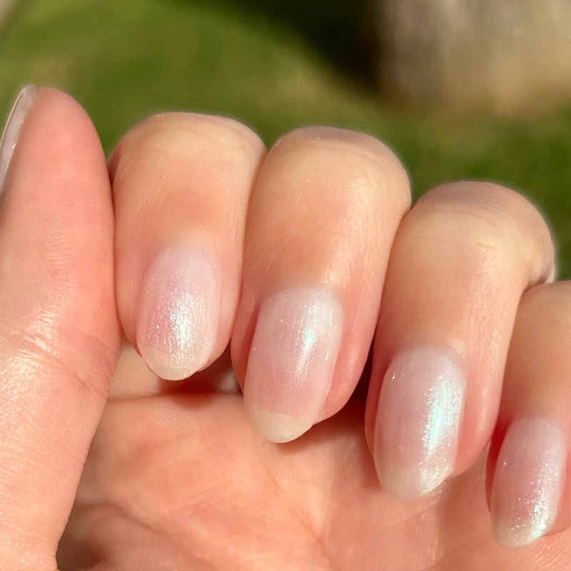 Hand with natural nails showing a sheer layered manicure in soft iridescent tones from the Freshwater Pearl Set