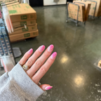 Hand wearing Ally Rooker Super Stick Set nails in pink gradient design with white streaks on a polished concrete floor background