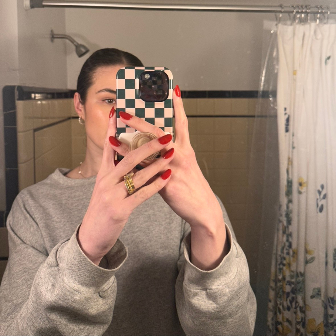Person wearing red nails using Ally Rooker Super Stick Set taking a mirror selfie in a bathroom with tiled walls