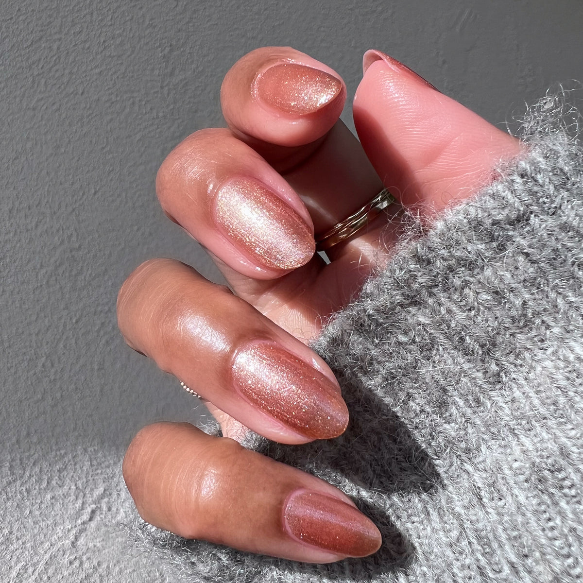 Hand with Penny polish showing a glossy copper metallic manicure on medium skin with natural sunlight and cozy sweater sleeve