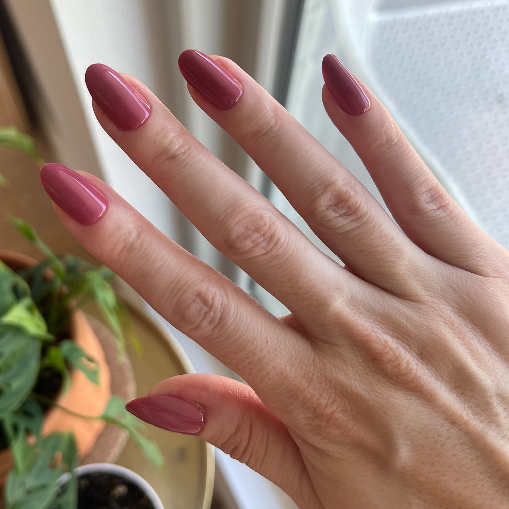 LD - Press-On | Medium | Oval showing hand with medium oval rosy press-on manicure indoors near plants and sunlight