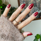 Hand with Brick polish showing smooth deep red manicure on natural skin with cozy brown sweater and indoor background