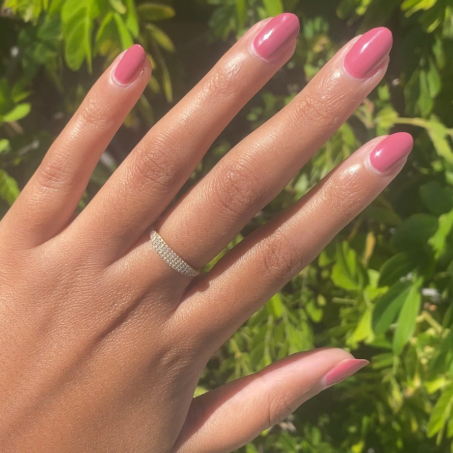Hand with nails painted in Primrose warm rosy pink gel polish showing a smooth polished manicure outdoors