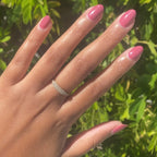 Hand with nails painted in Primrose warm rosy pink gel polish showing a smooth polished manicure outdoors