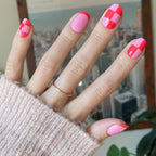 Pink Checker Party | Short | Round - Tab Press-On showing hand with pink and red checker and solid design false nails indoors