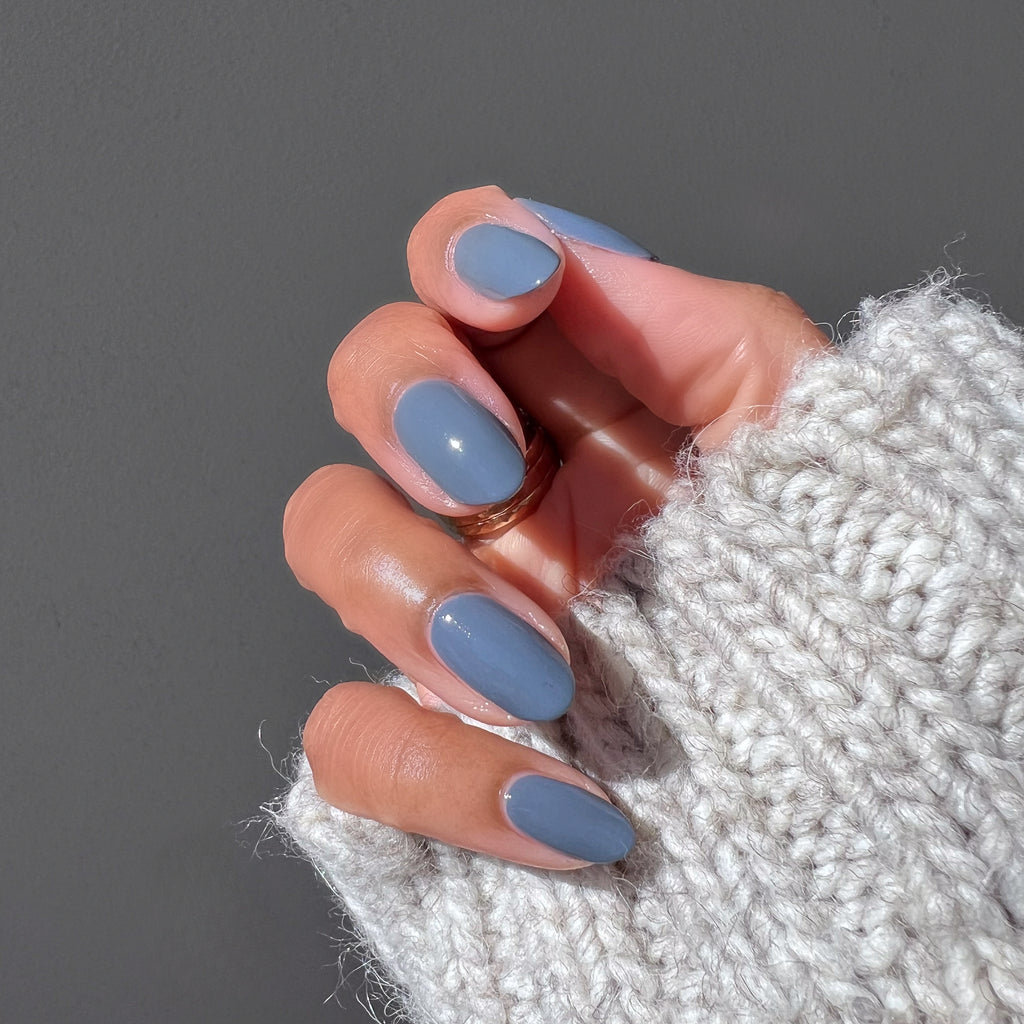 Hand wearing cozy knit sleeve with neatly done Favorite Beanie gel polish manicure in soft slate grey shade