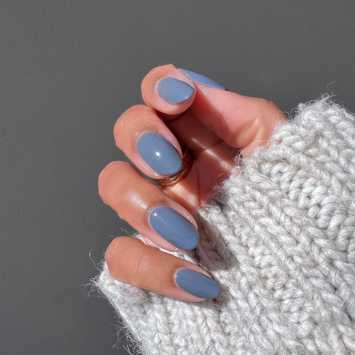 Hand wearing cozy knit sleeve with neatly done Favorite Beanie gel polish manicure in soft slate grey shade