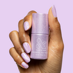 Hand with nails painted in Amethyst Velvet - Gel pastel lavender magnetic gel polish holding matching bottle against light purple background