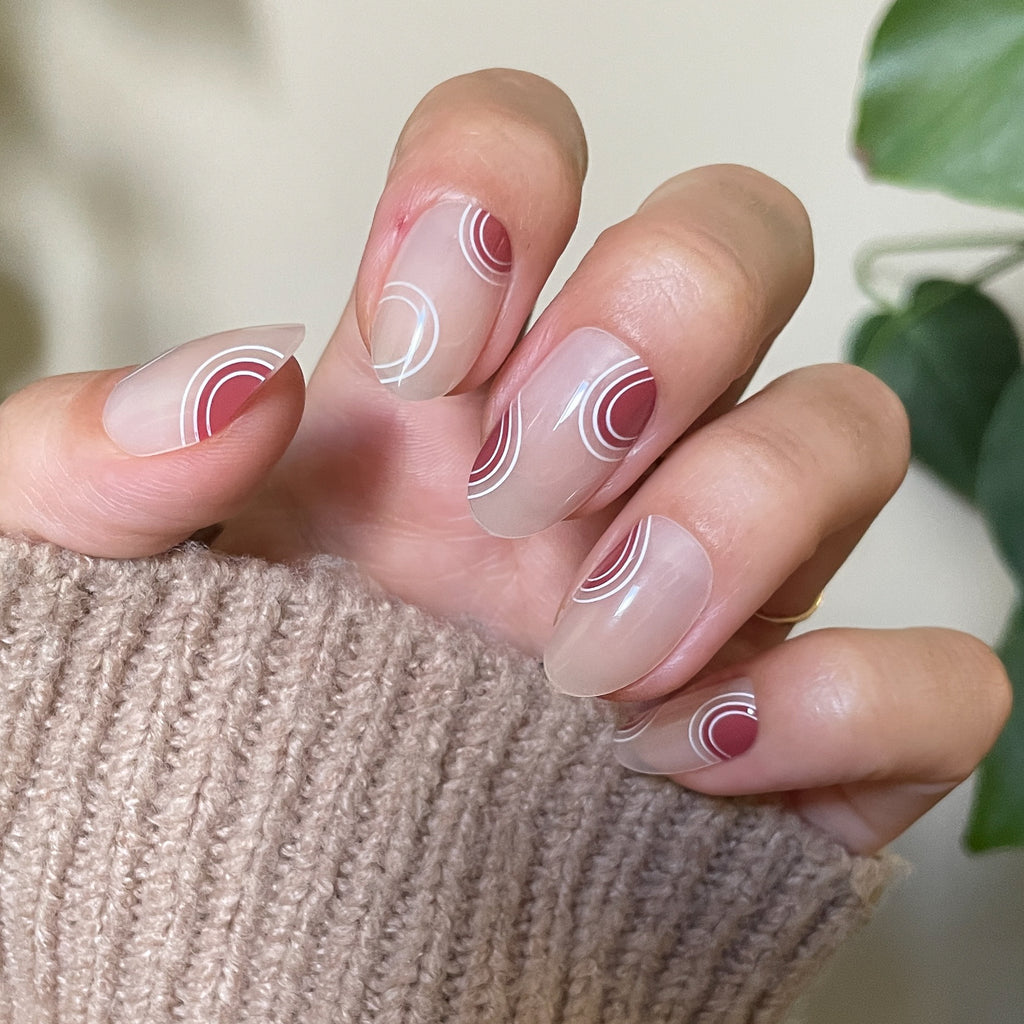 Layered Circles - Press-On | Medium | Oval neutral nails with burnt orange and white swirl accents on hand wearing beige knit sweater