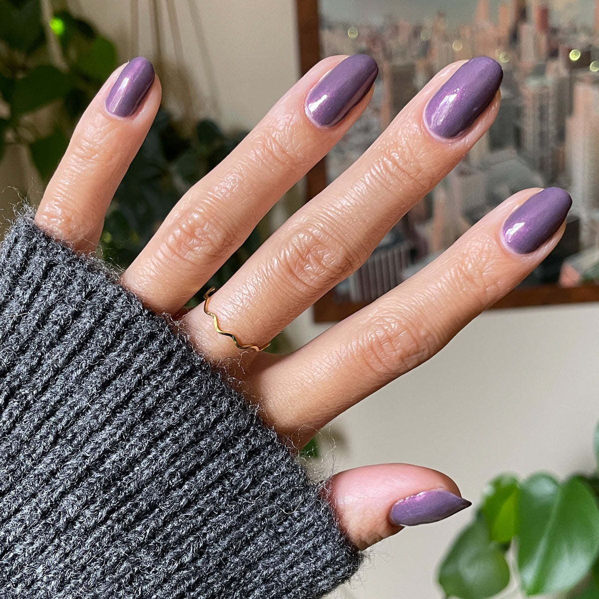 Hand with Twilight gel polish showing a shimmering violet manicure against a cozy indoor background