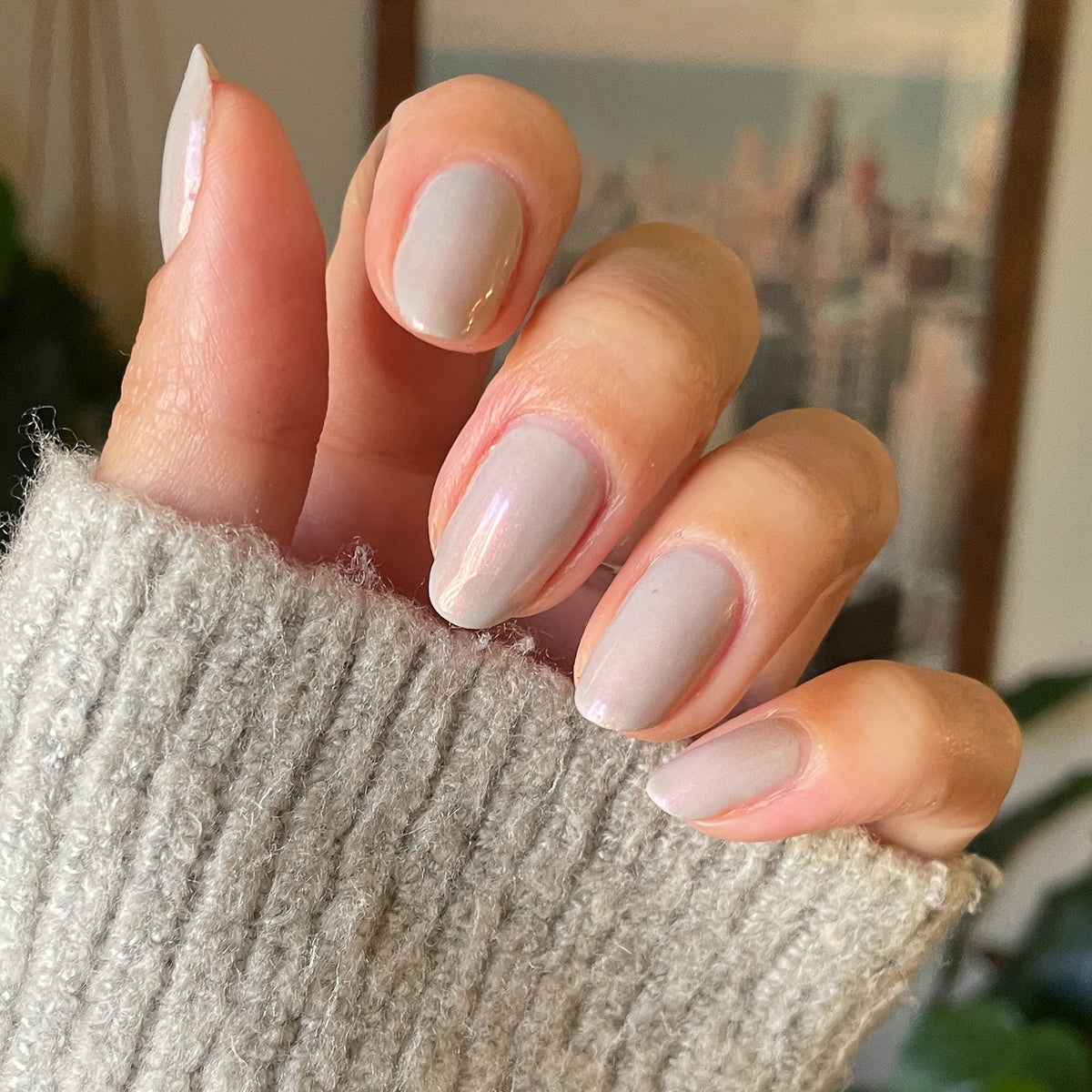 Hand with soft natural skin tone nails painted in iridescent milky grey Elevator quick dry polish for at home mani