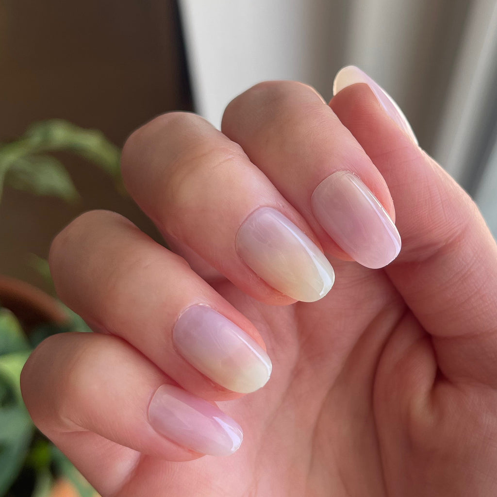 Tie Dye - Press-On | Short | Round showing close-up of hand with short round false nails in soft pastel gradient mani indoors near plants