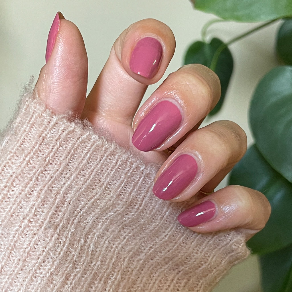 Hand with smooth, glossy Primrose gel polish in warm rosy pink showing a fresh manicure over knit fabric